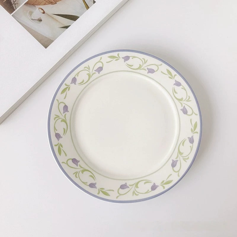 A white ceramic plate with a floral pattern, featuring a central tulip design, surrounded by a pink border with more floral accents